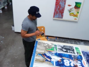 Image shows man working on a painting in a studio