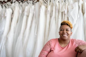 Image shows a woman sitting on a couch in a wedding gown shop.