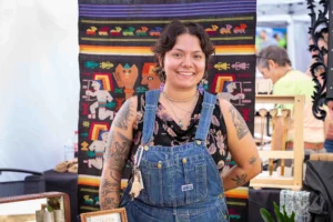 Image shows smiling woman in front of a hanging woven tapestry