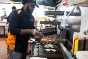 Man preparing a hot sandwich over a kitchen grill inside a busy restaurant