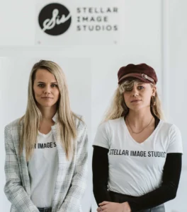Two blonde women sitting beside each other in a large white room.